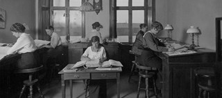 Sex kvinnor sitter vid skrivbord och skrivpulpeter och arbetar