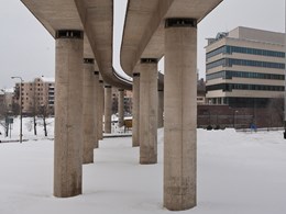 Betongbro på pelare, snö på marken och byggnader i bakgrunden