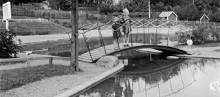 Bilden föreställer två barn som står på en liten bro över en plaskdam i en park 1940.