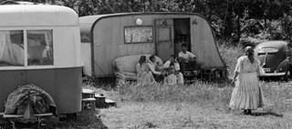 Personer som sitter och står framför en husvagn en sommardag