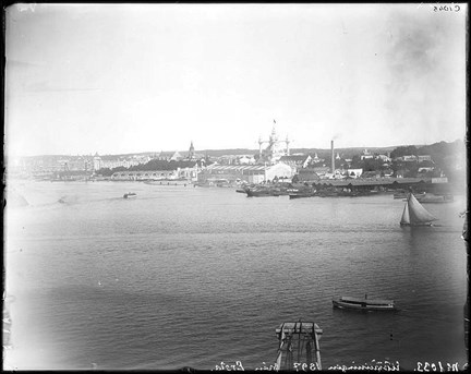 En utsikt över vattnet mot Djurgården och Allmänna konst- och industriutställningen 1897. Till höger i bild en segelbåt, i bakgrunden diverse utställningsbyggnader