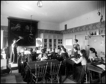 Flickor i klassrum, en lärare visar skisser på en tavla.