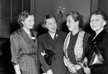Fyra kvinnor står och samtalar. Kvinnan längst till höger ler mot kameran.