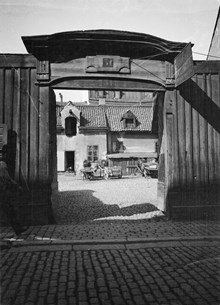 Stora Badstugatan 31. Vy genom porten i planket mot gården där några hästar är uppställda