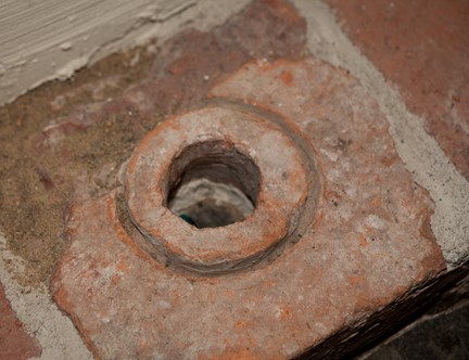 Bilden visar en medeltida hypocaust som är en tegelplatta med ett runt hål i mitten.