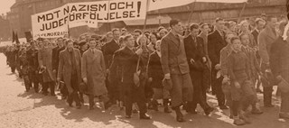 Människor går i demonstrationståg. En banderoll med texten "Mot nazism och judeförföljelse.
