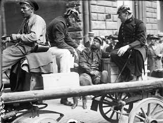 Svartvitt fotografi där en berusad man och två poliser i pickelhuvor sitter på en vagn