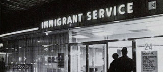 Svartvit kvällsbild på entrén till Immigrant service med en lysande neonskylt 