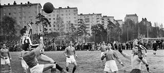 Män spelar fotboll på en gräsplan med höghus i bakgrunden
