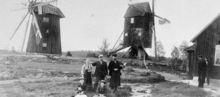 Några människor står uppställda framför två väderkvarnar vid sekelskiftet 1900.