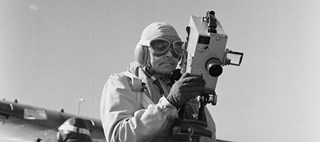 En person med skyddskläder och skyddsglasögon håller i en filmkamera