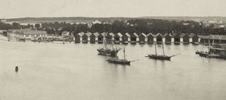 Bilden föreställer små hus som ligger vid vattnet och är en del av en varvsmiljö.