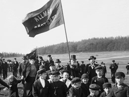 Svartvitt fotografi som visar barn och vuxna som demonstrerar för allmän rösträtt på ett fält, 1901.