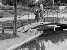 Bilden föreställer två barn som står på en liten bro över en plaskdam i en park 1940.
