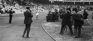 Målgång i 10 000 meter gång. En fotograf står vid mållinjen och en vitklädd löpare är på väg fram på banan inne på Stockholms stadion