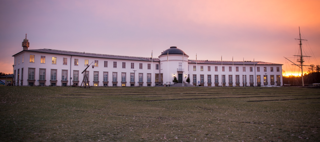 Bilden förestället ett vitt, längt, böjt hus i morgonljus.