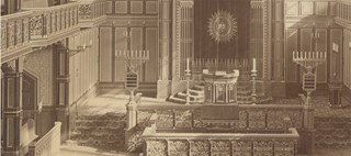 Interiör av synagoga med läktare, rosettfönster, bänkar och stora sjuarmade ljusstakar