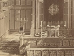 Interiör av synagoga med läktare, rosettfönster, bänkar och stora sjuarmade ljusstakar