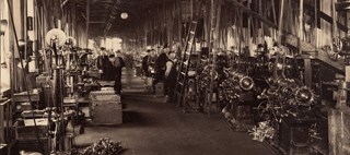 Arbetare står vid maskiner i en fabrikshall