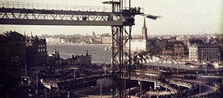 Fotografi som visar Slussens invigning 1935, Katarinahissen i förgrunden och folkmassor längs vägarna i trafikkarusellen