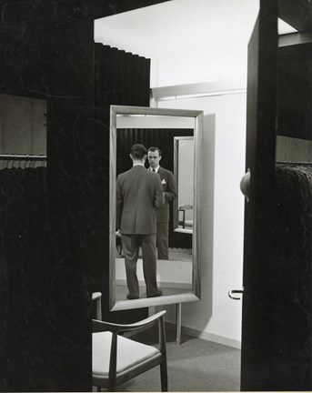 Svartvit bild på en man som speglar sig i ett provrum. 