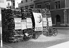 Vedstapel med valaffischer från Arbetarepartiet socialdemokraterna och Högern, samt en affisch från Gröna Lund