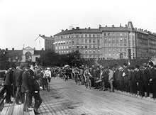 Gamla Liljeholmsbron, Hornstull. Starten för velocipedåkningen (cykeltävlingen) Mälaren runt. I bakgrunden syns Stockholms södra stadsport med tullhusen invid. Valvet revs 1905.