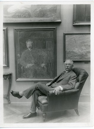 Tor Hedberg sittandes i en fåtölj med sitt porträtt på väggen bredvid sig.