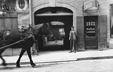 En häst passerar portgången till Drottninggatan 77. Till höger butiken Samuelssons bröd