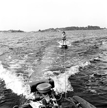 Flicka åker vattenbräda efter motorbåt med utombordsmotor. Stockholms norra skärgård