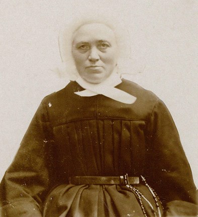 Porträtt i svartvitt av syster  Solina Margareta Ziegenfuss. Hon har ett runt ansikte och är klädd i svart dräkt, med vit hätta som täcker hela håret. Hättan har krusade kanter och under hakan en stor vit rosett.