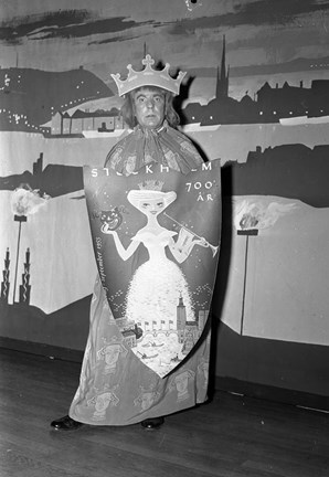 Mannen har bär en stor krona och en sköld med en bild av en kvinna och texten "Stockholm 700 år".