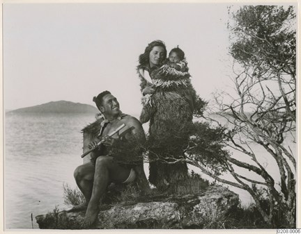 På en klippa: en man med en flöjt, och en kvinna med ett litet barn, alla tre i traditionella kläder.
