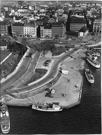 Flygfoto över vatten, kaj, båtar, vägar och i bakgrunden flervåningshus.
