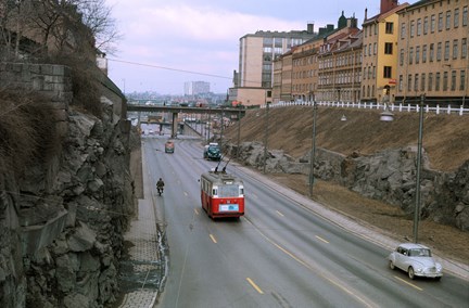 En gata med gles bil- och busstrafik, på ömse sidor berg och byggnader.