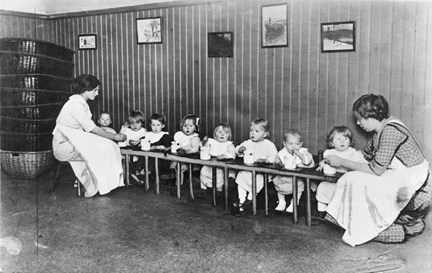 Interiör från Engelbrekts barnkrubba med små barn som av barskötare får hjälp att äta.