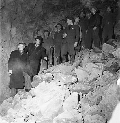 Ett par män i rock och hatt och andra i arbetskläder står i en lutande hög bortsprängd sten.