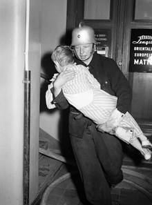 Mäster Samuelsgatan 46. Brandman bär ut 7-åriga Karl Gustav Harald. Eldsvåda uppstod i huset efter att en brottsling, en dynamitard, försökt spränga ett kassaskåp i ett försäljningskontor.