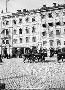 Några hästfordon står på Gustav Adolfs Torg utanför Hotell Rydberg vid Gustav Adolfs Torg 16. Kvarteret revs 1913 för Skandinaviska Bankens palats. Nuvarande Gustav Adolfs Torg 22-24
