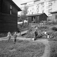 Kv. Ruddammen mellan Körsbärsvägen och Valhallavägen. Dam pumpar vatten vid nödbostäderna, barn leker på gården