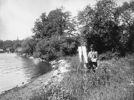 Fotografi av prins Eugen som står och målar vid staffli vid Ryssvikens vatten på Waldemarsudde ca 1910. 