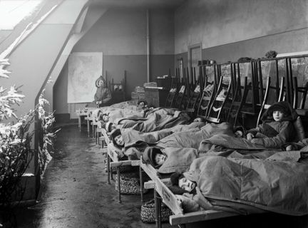 ett antal väl påklädda barn ligger och vilar på en takterrass i enkla träsängar