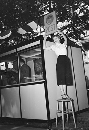 En kvinna står på en pall och håller upp en postskylt intill det tillfälliga postkontoret.