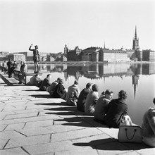 Stadshusträdgården. Stockholmare har i vårvärmen sökt sig till stadens vatten och slagit sig ner vid Stadshuset. Vy mot Riddarholmen. Skulpturen till vänster är Carl Eldhs ""Sången""