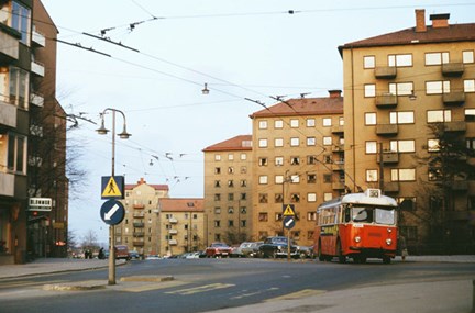 En röd buss kör på en gata mellan bruna hus