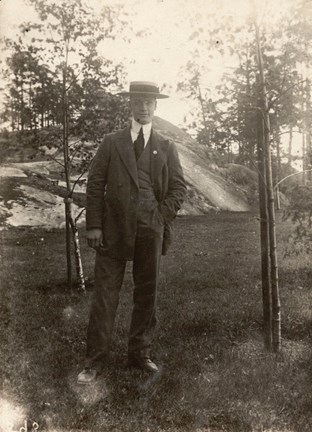 Foto av "Manne Anderberg" i kostym stående i en träddunge.