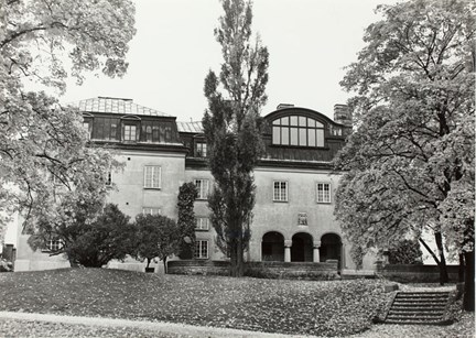 Fotografiet visar Slottet på Waldemarsudde sett från norr med parkens växtlighet och gångvägens trappa upp till huvudentrén i förgrunden.