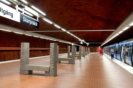 Vy över perrongen på Skarpnäcks tunnelbanestation med granit skulpturer i form av bänkar och ett tunnelbanetåg 