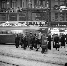 Stureplan 2-4. Folk väntar på buss/spårvagn i snöyran. I bakgrunden syns Hedengrens Bokhandel, Göteborgs Bank och Fröjds Herrkläder