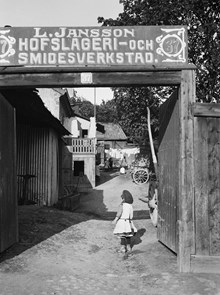 En liten flicka står i portöppningen till gården vid Nytorget 37. Här finns L. Janssons hovslageri och smidesverkstad. Nuv. Nytorget 3